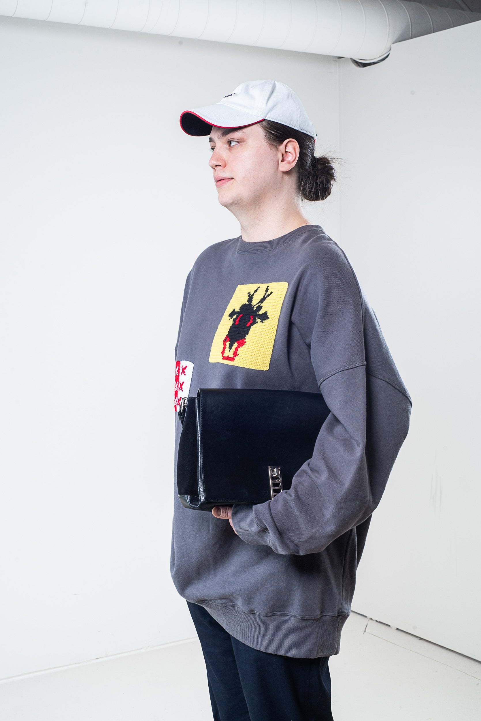 Model wearing J.W. Anderson Grey Patch Knit Sweater, side view, carrying a bag

