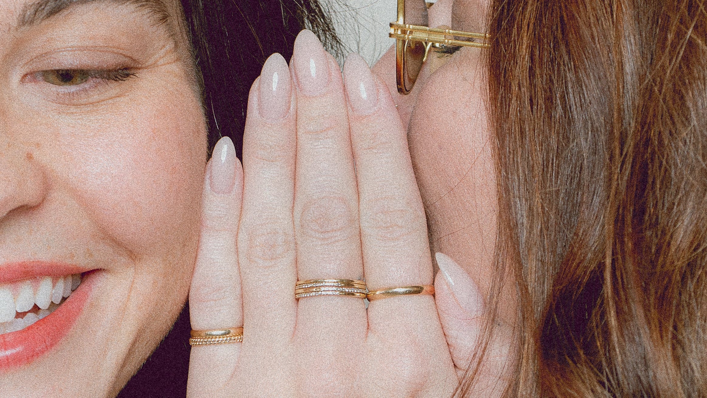 Two women with one whispering into the other's ear, wearing gold rings.