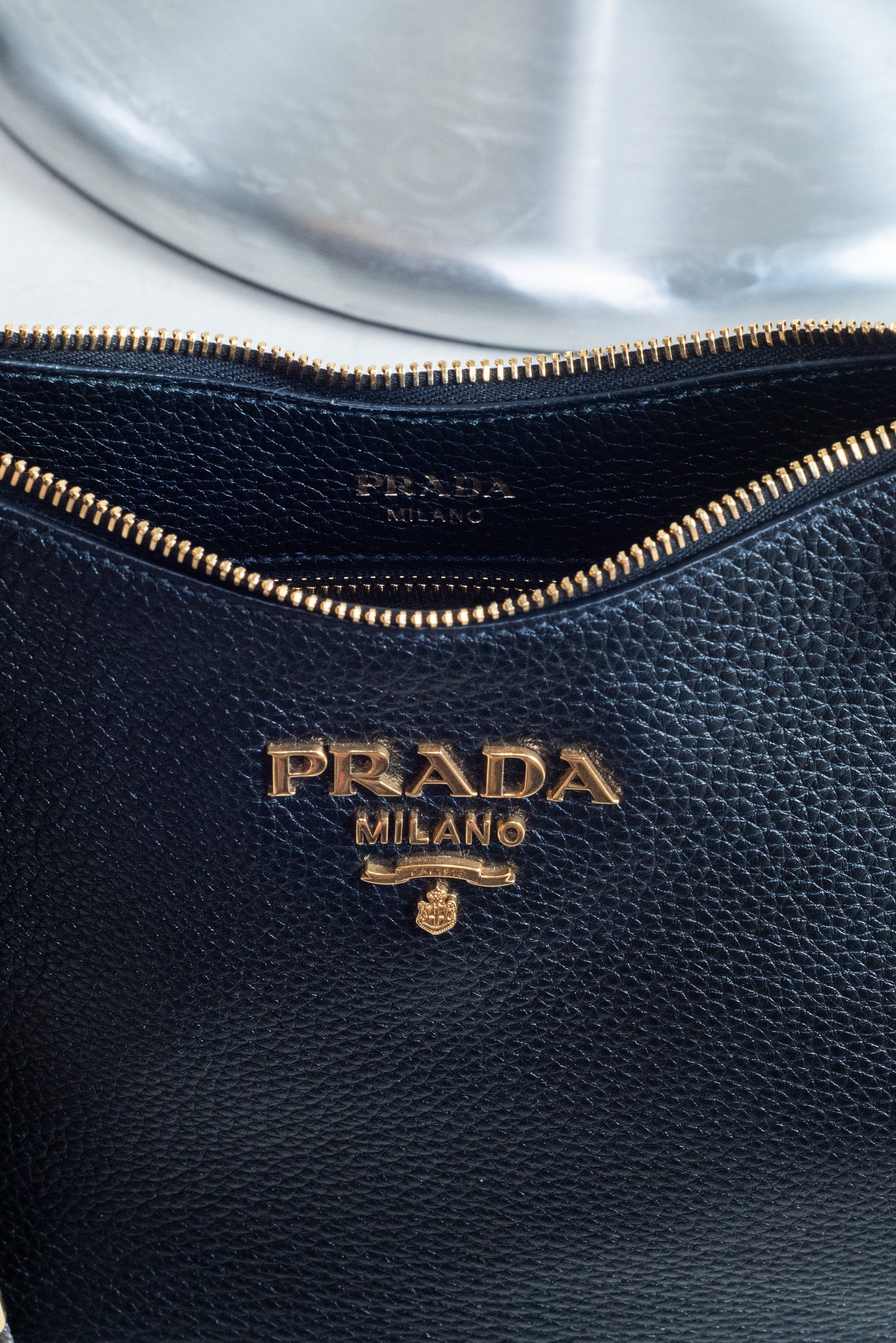 Detailed view of the gold-tone zipper on the Prada Black Vitello Leather Crossbody Bag